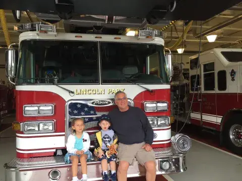 A man and two kids pose in front of a fire truck.
