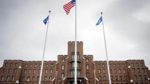 Front facing wide angle of the St. Elizabeth's Campus building. The road is covered in snow. Three flag poles stand in triangle formation in front of the building.